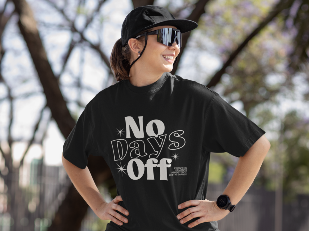02 Fitness and gym culture A woman with a ponytail wears a black cap and mirrored sunglasses, smiling confidently. Her black t-shirt reads "No Days Off".