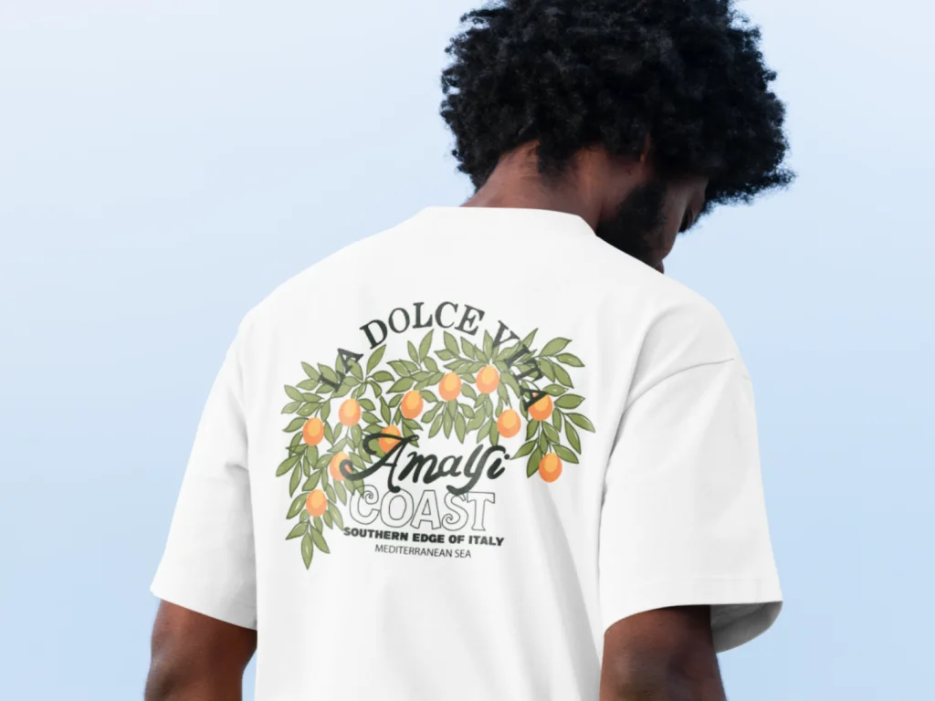 03 Travel inspired designs Man wearing a white t-shirt with a design of orange branches and leaves. Text reads "La Dolce Vita, Amalfi Coast”.