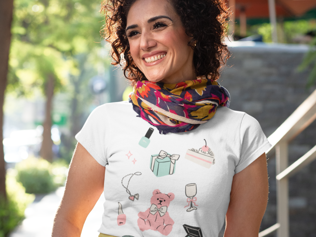 05 Handwritten doodle style graphics Smiling woman outdoors, wearing a white t-shirt with colorful doodles of makeup, a gift box, cake, and a scarf.