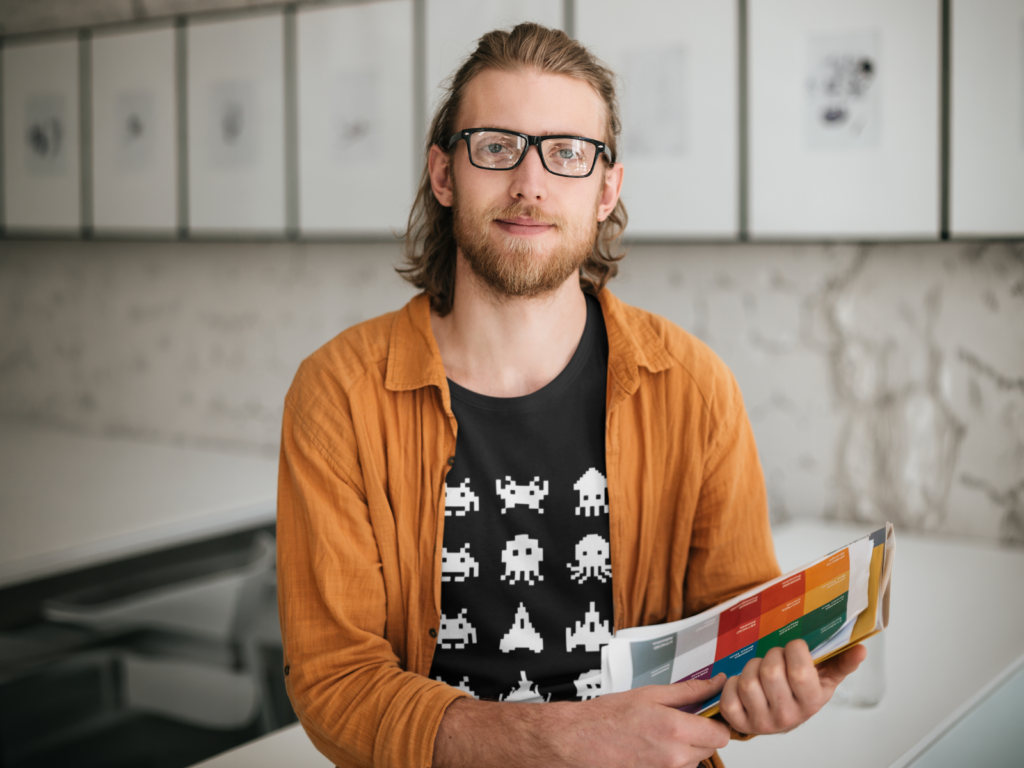 10 Gaming meme and geek culture A man with glasses and a beard smiles while holding colorful charts. He wears a black shirt with white space invaders and an orange jacket.