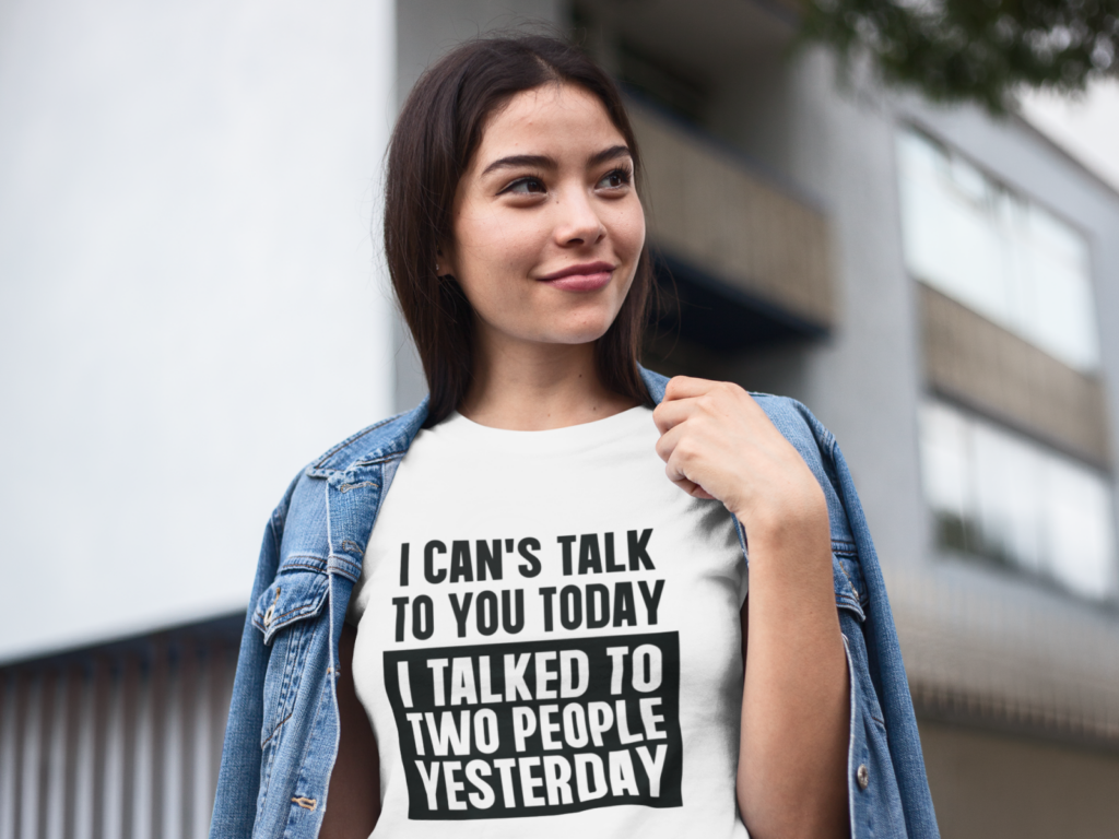 11 Digital minimalism and introvert humor Woman outdoors, smiling and wearing a denim jacket over a white "I can't talk to you today, I talked to two people yesterday" tee.
