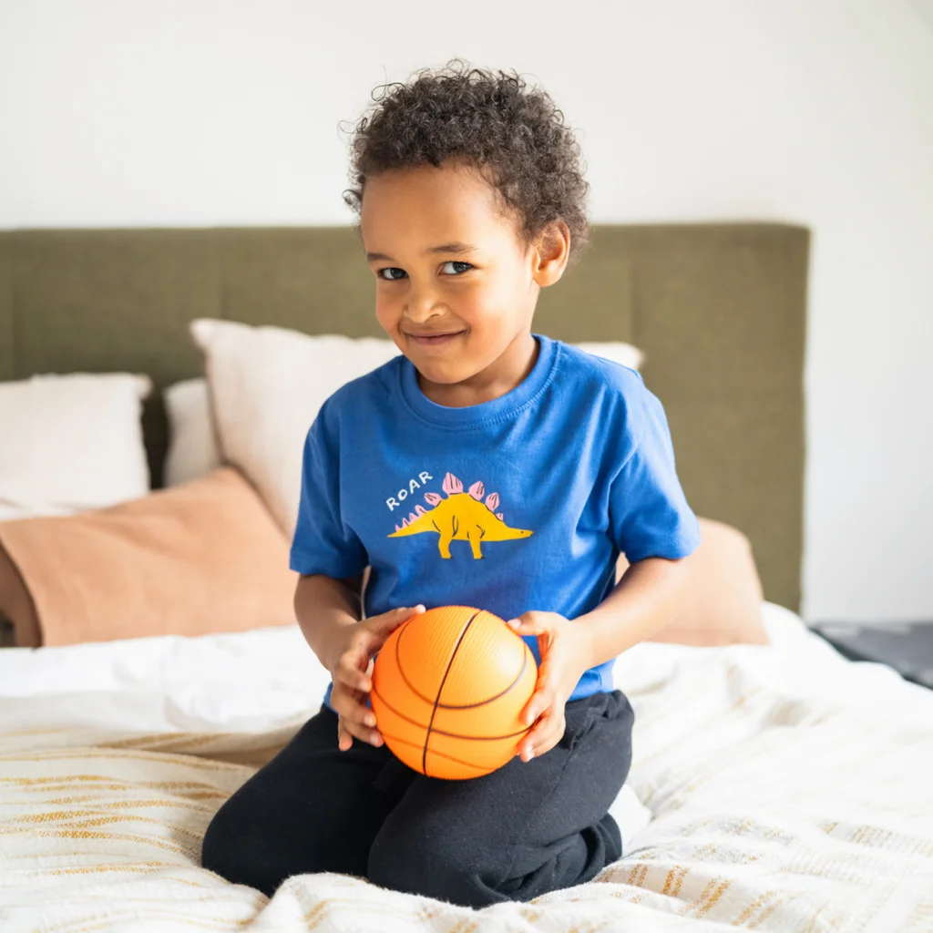 Baby apparel A young boy playing with a basketball wearing a custom blue “Roar” t-shirt with a dinosaur print.