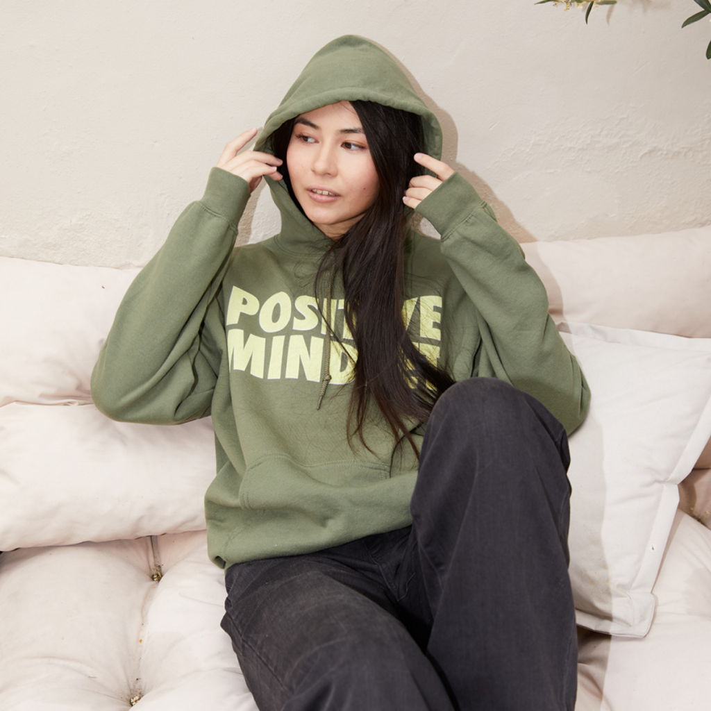 Custom hoodies A woman in a custom “Positive Mindset” hoodie on a white couch.