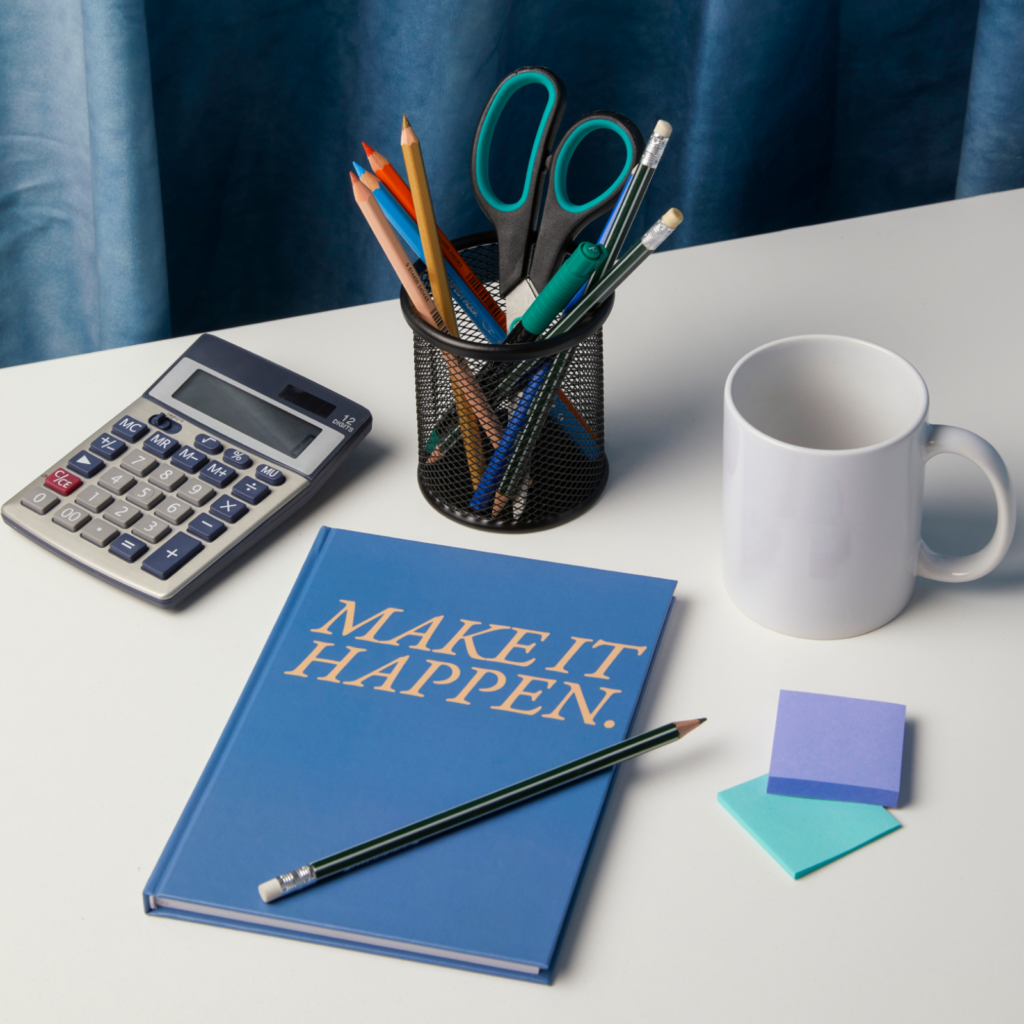 Custom notebooks and journals A custom "Make It Happen" notebook, pencil, calculator, coffee mug, notepad, pen, and notebook arranged on a white table.