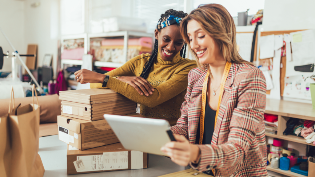 Set up your online store Two women in a professional setting engaged in discussion over a tablet.