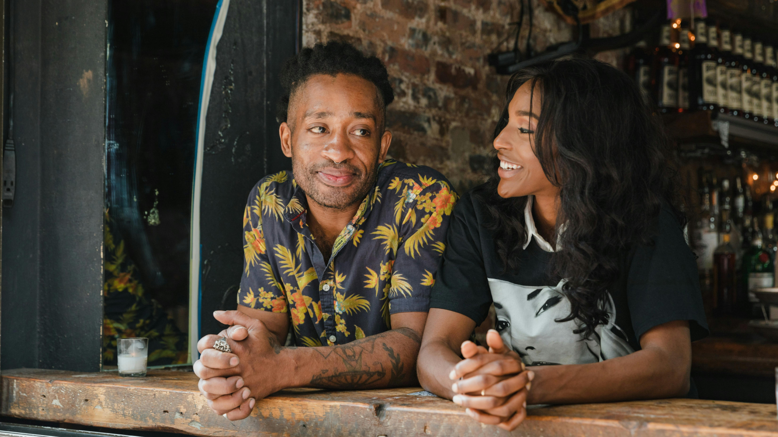 What is an all over print shirt A man in a vibrant all-over-print shirt and a woman sit at a bar, engaged in friendly conversation.
