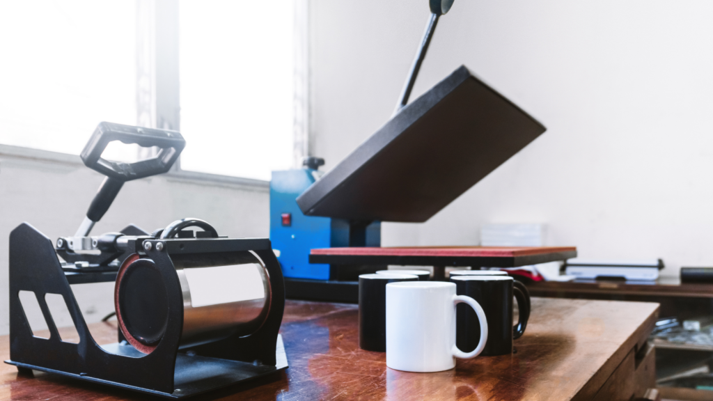 What is sublimation Understanding the science Heat press machine with open platen on a wooden table, next to a mug press holding a white mug.