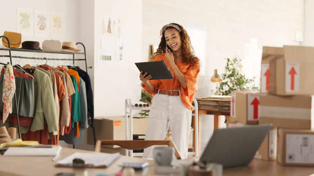 Why start an embroidery business A woman stands before a desk cluttered with boxes and a laptop, engaged in her work environment.